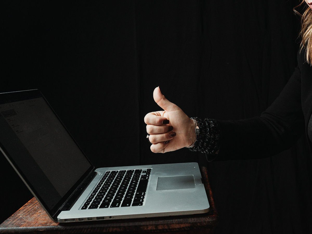 Persona usando un computador portátil aprueba con el pulgar hacia arriba